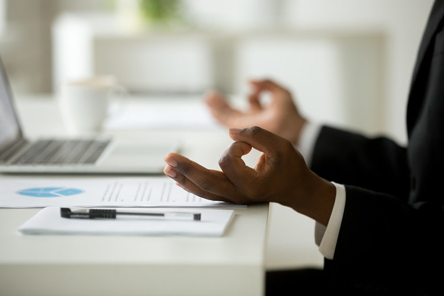 African american calm businessman relaxing meditating in office, peaceful ceo in suit practicing yoga at work, focus on black man hands in mudra, successful mindful people habits concept, close up